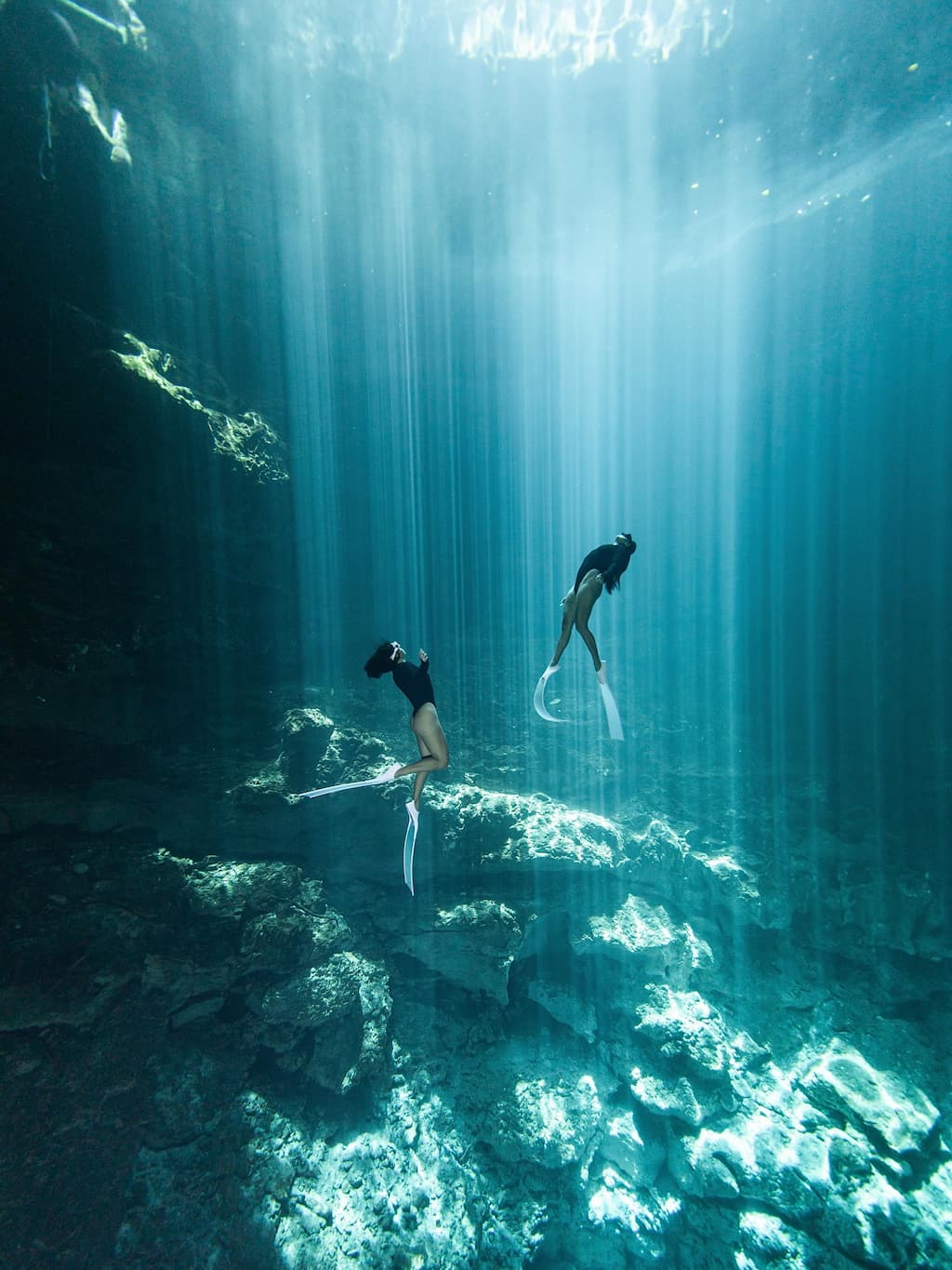 Two women divers in crystal-clear turquoise cave water inside Cenote Dos Ojos